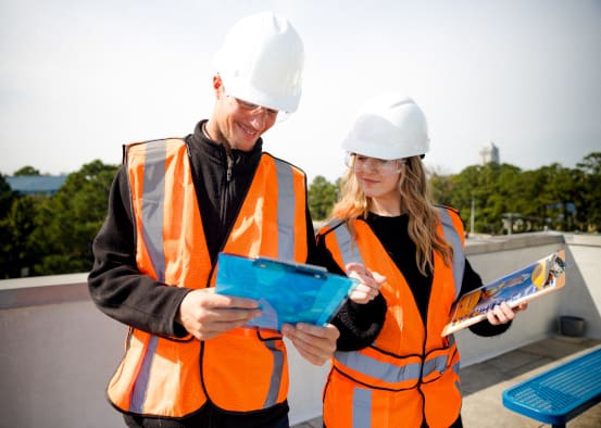 Two solar technicians looking at plans on the roof of a building